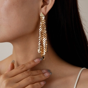 Macro view of gold geometric mesh tassel earrings on a model showing metallic texture