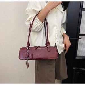 Detail of dark red leather baguette bag with a bow charm worn as an underarm shoulder bag