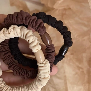 Three premium ribbed fabric scrunchies in brown black and beige held in hand