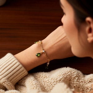Detail eines 18k vergoldeten Doppelarmbands mit grünen Tropfenanhängern und Edelsteinen