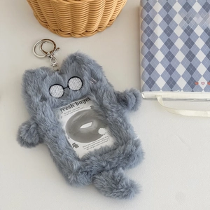 Detail of plush grey monster card holder with embroidery, glasses, and a metal keychain