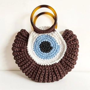 Detail of hand-woven shell bag showing unique eye pattern and amber round handles