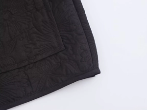 Macro detail of black jacket fabric featuring floral quilted pattern and textured finish