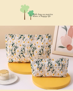 Close-up of quilted beige makeup bags with white daisy embroidery and woven logo label