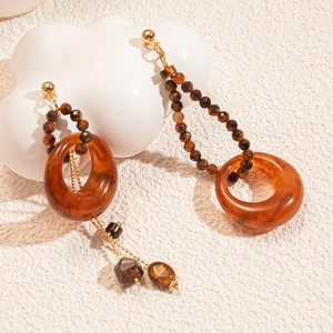 Detail of round tiger eye resin earrings on a beige textured fabric with a cloud prop