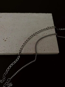 Detail showing two layered silver stainless steel chains on a textured stone