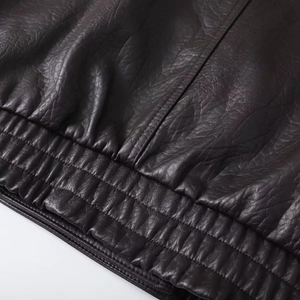 Detailed close-up of dark brown faux leather jacket with elastic hem and fine stitching
