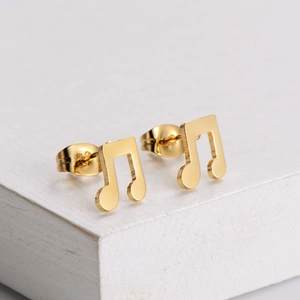 Polished golden music note stud earrings in stainless steel on white wooden background