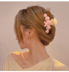Detail of a creamy hair claw clip with pink bear and hearts worn on a model's hair