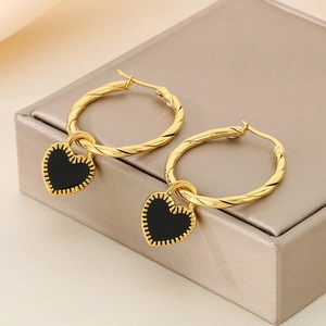 Detail of gold twisted hoop earrings featuring black enamel heart pendants on leather