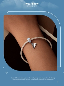 Silver mesh bracelet detail with blue flower charm and airplane pendant on wrist