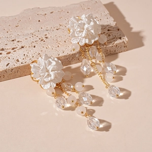 Detail of elegant white acrylic flower earrings with golden tassel and glass beads