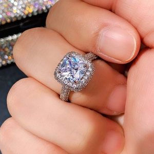 Macro close-up of square halo ring with clear gemstone and pavé band on finger