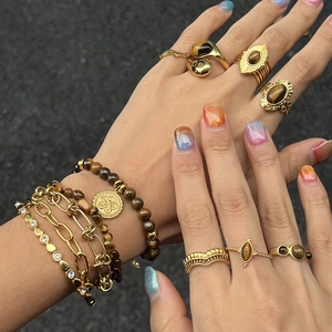 Gros plan de bagues œil-de-tigre et de bracelets dorés superposés sur une main