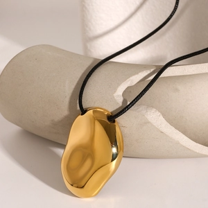 Minimalist gold pebble pendant on black cord necklace displayed on white geometric stone