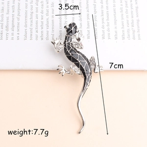 Fashionable silver lizard brooch with black enamel and rhinestones on book background