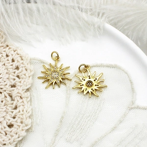 Detailed view of two gold sun pendants with cubic zirconia on a ceramic tray