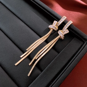 Close-up of golden tassel earrings with knot design and square cubic zirconia on leather