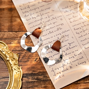 Close-up of bohemian geometric silver hoop earrings with brown textured leather accents