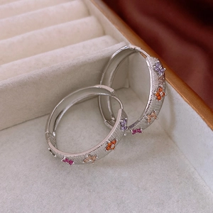 Detail of wide brushed silver earrings with colorful zircon floral pattern inlay