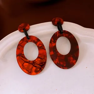 Minimalist red oval acrylic drop earrings with amber texture on white porcelain plate