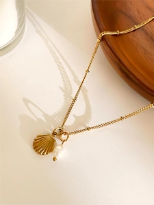 Macro shot of gold necklace featuring shell pendant and freshwater pearl on bright desk