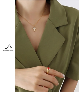 Detail of gold-tone cross necklace with pearls and gemstone ring on model in olive suit