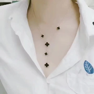 Dettaglio di una collana a quadrifoglio dorata con ciondoli neri su camicia bianca