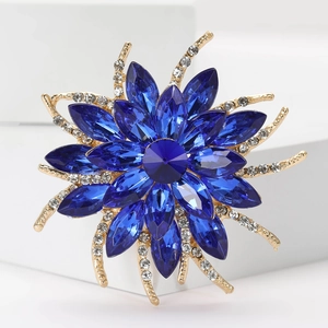 Radial blue flower brooch with crystals on a golden alloy base in a studio setting