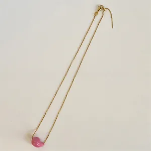 Detail of a gold-plated fine chain with a smooth pink bean pendant on white background