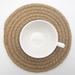 Close-up of a round jute braided placemat with a white ceramic tea cup on a white background