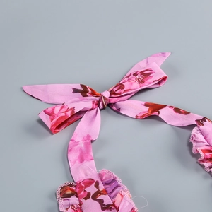 Detail of pink floral fabric dress featuring a delicate bow tie and ruffle edge design