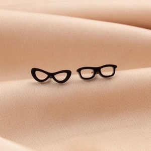 Macro shot of unique black sunglasses-shaped stud earrings on a soft beige background