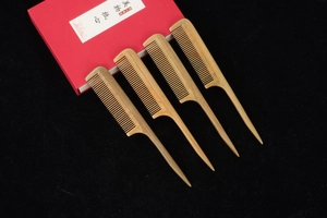 Set of four sandalwood hair combs with fine teeth and red gift box on black background