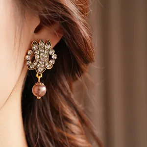 Vintage gold hollow earrings with zircon inlay and pearl pendant worn by a model