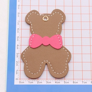 Detailed view of a brown leather bear keychain charm with a pink bow on a grid mat