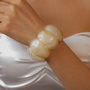 Detail view of a thick cream marble resin bracelet worn on a wrist with silk clothing