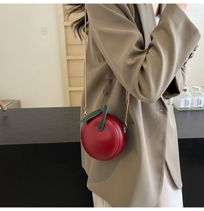 Detail of red apple shaped crossbody bag with gold chain strap on a khaki blazer