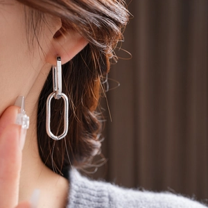 Close-up of stylish silver oval chain hoop earrings worn by a model in soft lighting