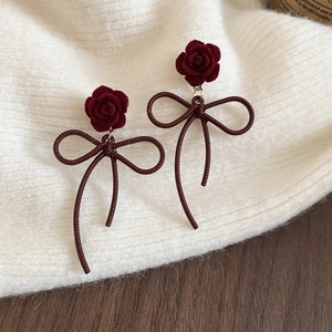 Close-up of velvet rose earrings with red metallic bow tassels on a white knit fabric