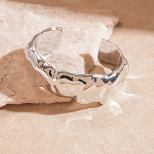 Detailed macro view of silver wavy textured bangle on a textured stone surface