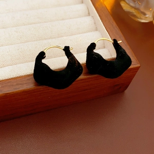 Close-up of black velvet irregular hoop earrings on a wooden jewelry display tray