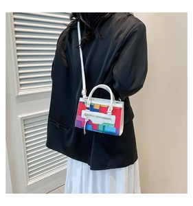 Detail view of colorful geometric patchwork handbag with white adjustable strap worn on shoulder