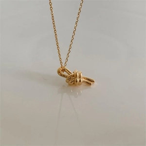 Detail of a minimalist gold knot pendant necklace with soft reflection on a warm surface