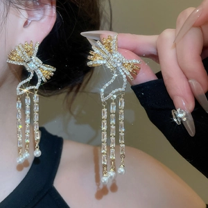 Close-up of golden bow earrings with long tassels, shiny cubic zirconia and white pearls