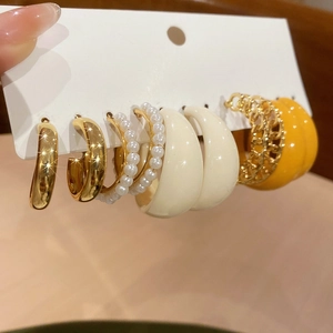 Détail de cinq boucles d'oreilles C en acrylique aux finitions dorées, crème et jaune vif