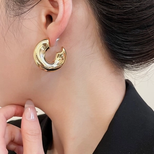Close-up of golden chunky C-shaped hoop earrings on a model showing polished metal texture