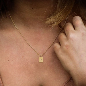 Close-up of a gold rectangle pendant necklace with a starburst pattern on a female model