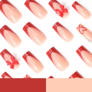 Faux ongles French avec nœuds rouges, motifs de cœurs et strass sur fond blanc épuré