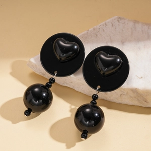 Detail of glossy black acrylic heart earrings with large spherical beads on stone base